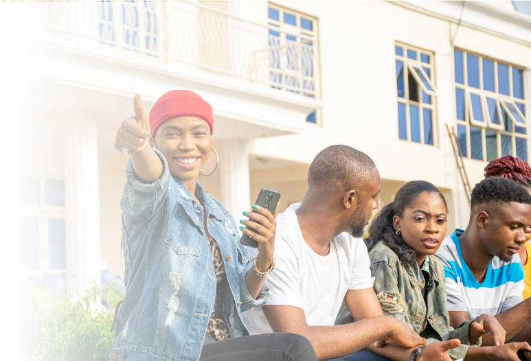 Homepage_Hero_image_faded A gathering of youth outside of a school. The woman in the foreground is smiling and giving a thumbs up sign