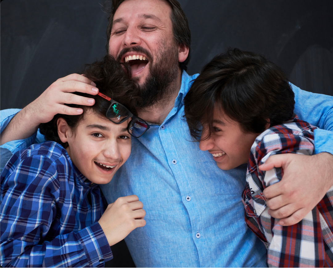 A smiling father hugs his two sons