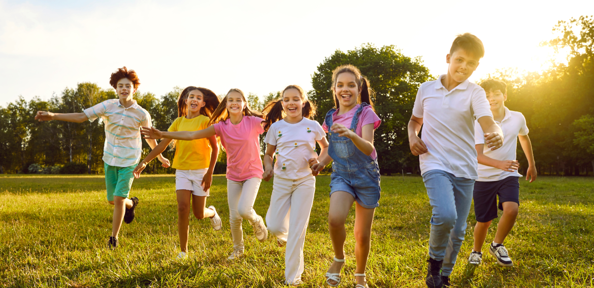 A group of seven joyful youths run on green grass in the summer