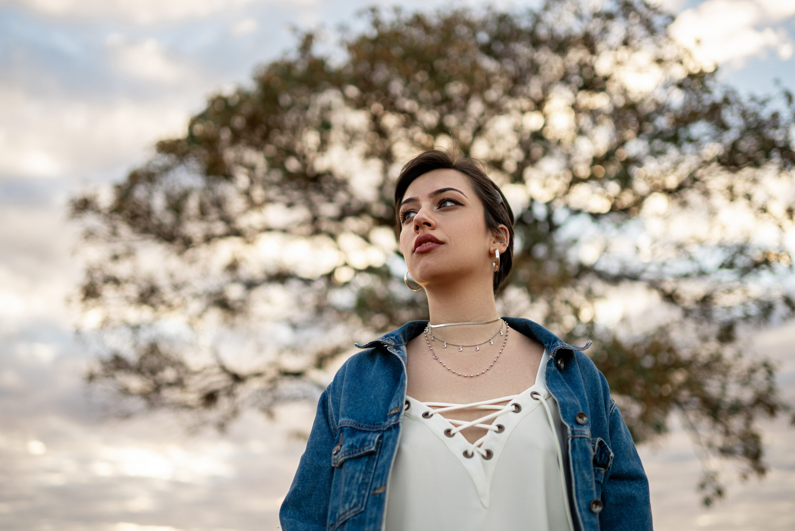 referayouth2 A young woman with short hair stands in front of a tall tree and looks into the distance