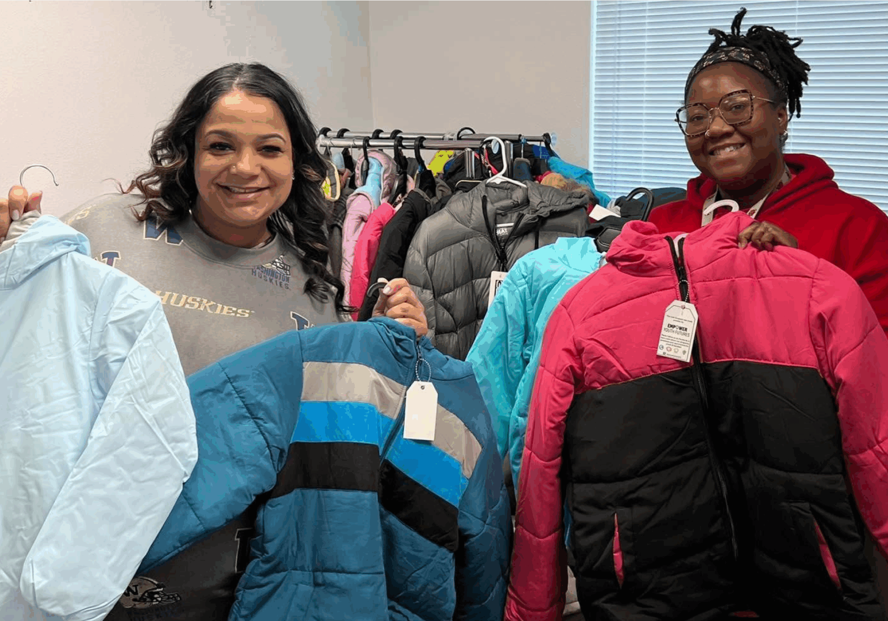 Echo Abernathy and a smiling youth hold up winter jackets
